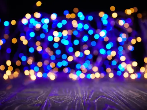 Luci blu e dorate creano un magico effetto bokeh su uno sfondo scuro, con un piano in legno in primo piano.