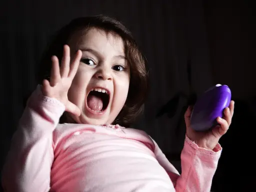 Niño asustado grita con la boca abierta, levantando una mano y sosteniendo un objeto morado.