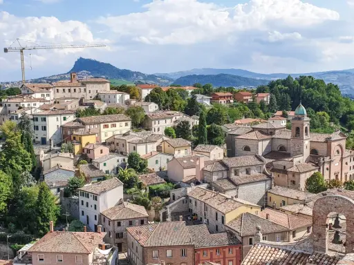 Un borgo pittoresco sulle colline riminesi, con tetti rossi, una chiesa con campanile e un paesaggio verdeggiante sullo sfondo.