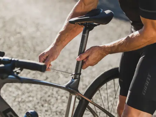 Rowerzysta reguluje wysokość siodełka w rowerze szosowym, używając klucza imbusowego.