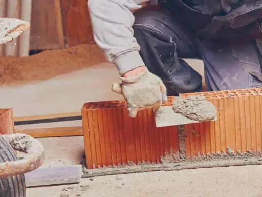 Murarz nakłada zaprawę murarską do bloczków betonowych na budowie.