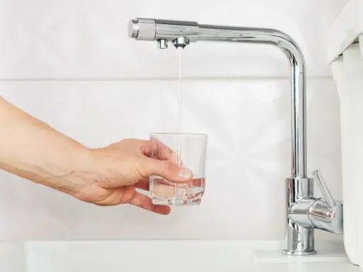 Main tenant rempli un verre d'eau sous un robinet de cuisine moderne, peut-être pour tester un nouveau joint mitigeur cuisine.