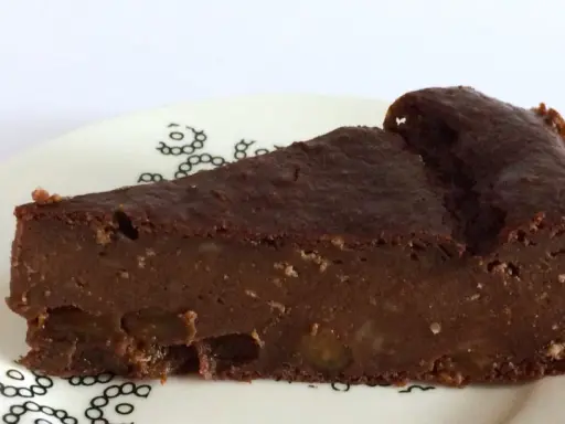 Una fetta di torta di pane al cioccolato, umida e ricca, con pezzi di frutta secca. La torta di pane ricetta della nonna, servita su un piatto bianco con decorazioni nere.