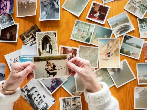 Mani anziane sfogliano vecchie foto stampate su un tavolo di legno, un modo per conservare le foto stampate e i ricordi.