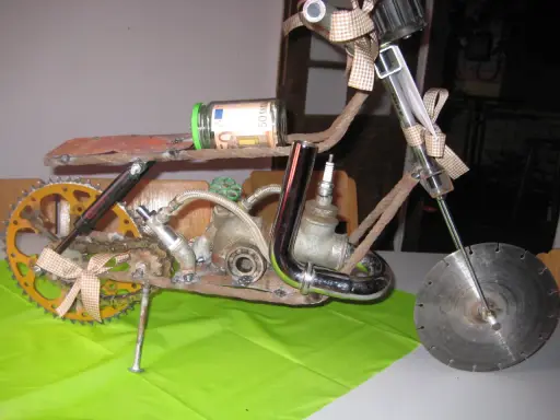 Kreatives Motorrad aus Altmetall, mit einem 50-Euro-Geldschein im Glas als Tank und einem kleinen Motorradhelm-Anhänger.