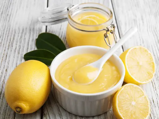 Aksamitny curd cytrynowy w miseczce, obok cytryny i słoiczek z tym pysznym kremem. Idealny do deserów!