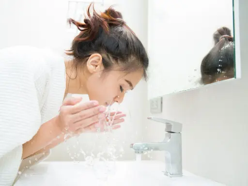 Une jeune femme se lave le visage le matin, sous un jet d'eau fraîche. Une routine beauté essentielle pour se réveiller.