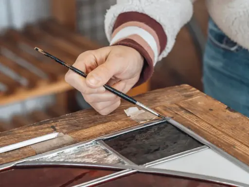 Main d'un artisan travaillant sur un vitrail, un exemple de métiers rares et recherchés.