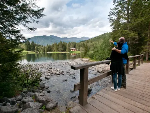 Coppia ammira il lago dei caprioli, con montagne sullo sfondo e una casa tra gli alberi.