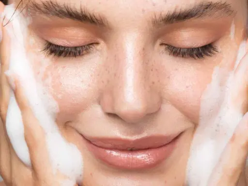 Une femme au visage frais, les yeux fermés, savoure la mousse d'un nettoyant. La définition de la pureté.