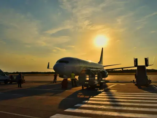 Samolot flydubai na lotnisku o zachodzie słońca. Pracownicy przygotowują bagaż rejestrowany, sprawdzając jego wymiary przed załadunkiem.