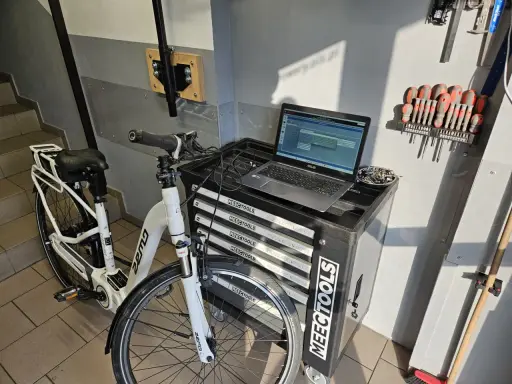 Profesjonalna naprawa rowerów elektrycznych w warsztacie. Biały rower elektryczny, laptop z oprogramowaniem diagnostycznym i zestaw narzędzi.
