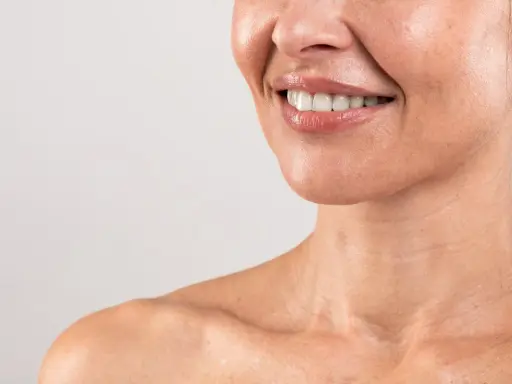 Sorriso radioso con labbra lucide e denti bianchi. La pelle del collo mostra le delicate "collane di Venere", segni di bellezza naturale.