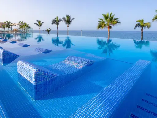 Piscina a sfioro con lettini integrati e palme, vista mare. Un sogno al searesort Riu Gran Canaria.