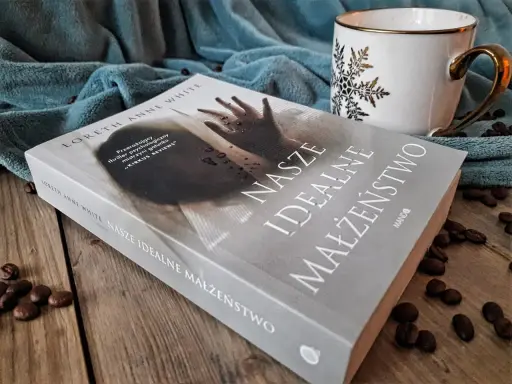 Książka "Nasze idealne małżeństwo" na drewnianym blacie, obok filiżanki i ziaren kawy.