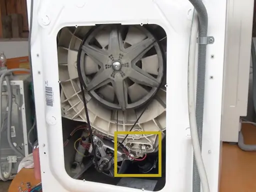 Innenleben einer Waschmaschine mit Riemenscheibe und Motor. Gelber Kasten markiert Bauteil, das bei einer Waschmaschine Unwucht verursachen könnte.