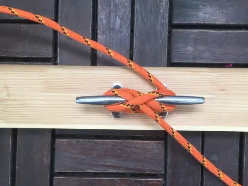 Pomarańczowa lina z żółtymi i czarnymi paskami tworzy solidny knaga węzeł na metalowym knadze.