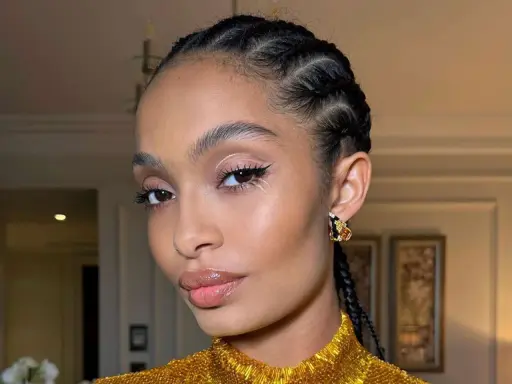 Primer plano de una mujer con trenzas, maquillaje de ojos con delineado y brillo, y labios brillantes.
