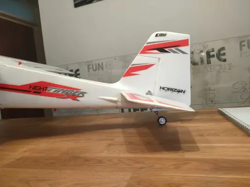 Modellflugzeug mit Aufschrift "NIGHT TIMBER" und "Eflite" Logo. Das Flugzeug steht auf einem Holztisch, bereit zum Flug.