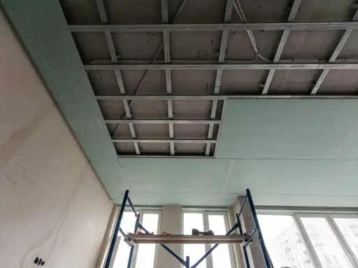 Instalación de falso techo de pladur para aislar techo ruido vecinos. Andamio y estructura metálica visibles.