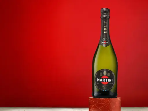Butelka Martini Brut 7.5% alc. vol. na tle czerwonej ściany.