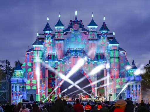 Castillo de luces y regalos en el parque navidad Torrejón. Artistas actúan en un escenario frente a la multitud.