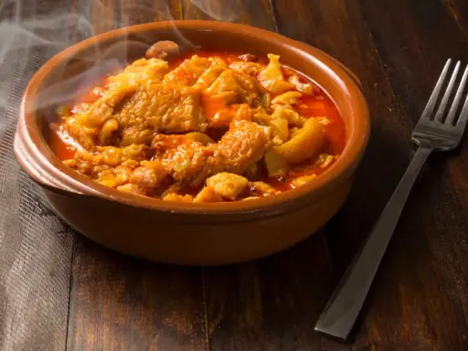 Un plat fumant de tête de veau mijotée, rappelant la recette tête de veau grand mère, servi dans un bol en terre cuite avec une fourchette.