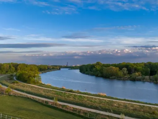 Wisła, jaka rzeka płynie przez Kraków, meandruje wśród zieleni. W oddali widać miejską panoramę.
