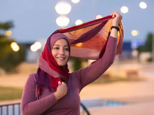 Lächelnde muslimische Frau mit buntem Hijab und Schal, der im Wind weht. Ein Bild, das die Vielfalt und Schönheit islamischer Kultur zeigt.