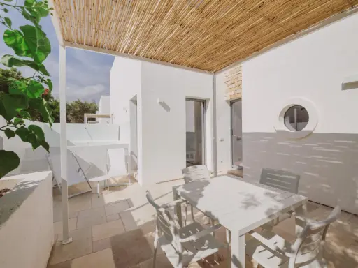 Terrazza con tavolo e sedie bianche, tettoia in bambù, tipica del Nicolaus Club Meditur Village.