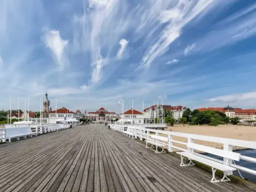 Drewniane molo w Sopocie, z widokiem na plażę i zabytkowe budynki. To popularne sopockie atrakcje, idealne na spacer.