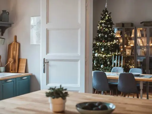 Julstämning i köket med en öppen dörr som avslöjar ett vackert julpyntat träd och en matsal. Perfekt jul inredning inspiration.