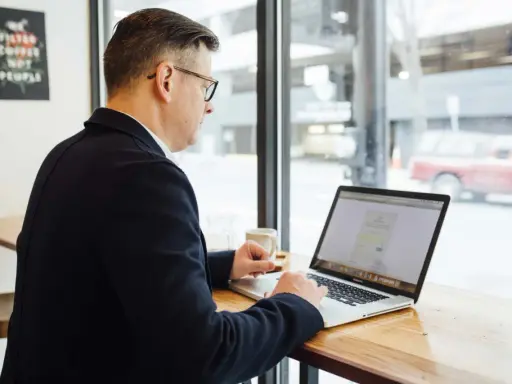 Hombre revisa en su laptop una cotización a tiempo parcial a efectos de jubilación, sentado en una cafetería.