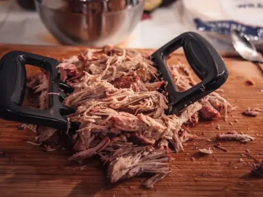 Pulled pork mit Fleischgabel auf Holzbrett. Perfekt für Smoker Rezepte Schwein, z.B. Pulled Pork Sandwiches.