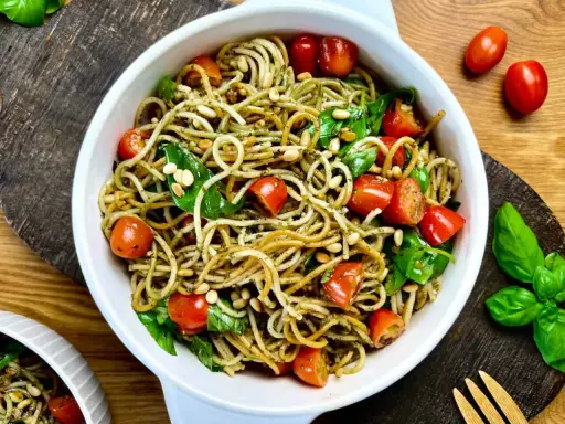 Leckerer Spaghetti-Salat zum Grillen mit Kirschtomaten, Pinienkernen und frischem Basilikum in einer weißen Schüssel.