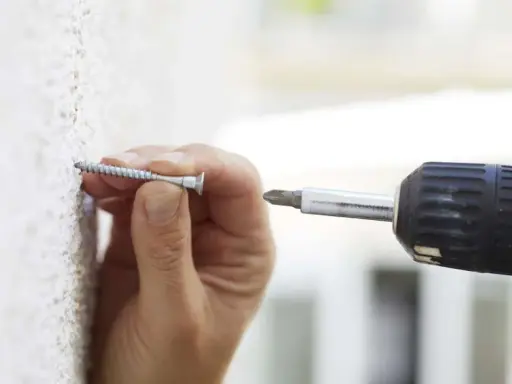 Mano insertando un tornillo en una pared texturizada, útil para saber si una pared es de pladur.