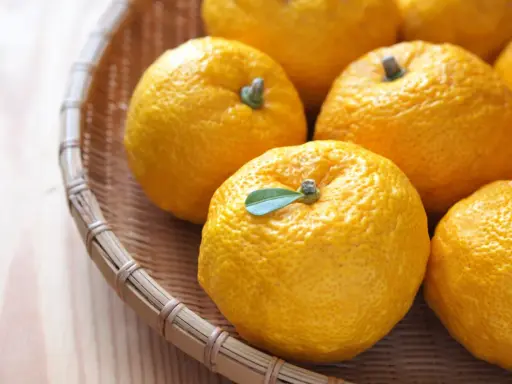 Kilka żółtych owoców yuzu w wiklinowym koszyku. Zastanawiasz się yuzu co to? To cytrus o intensywnym aromacie.