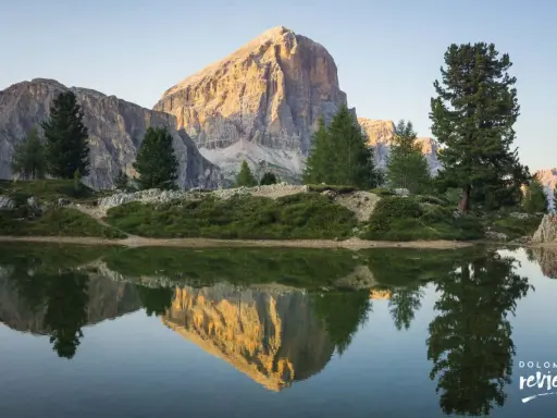 Riflesso perfetto di una montagna imponente nel lago di Limides, con alberi verdi e cielo azzurro.
