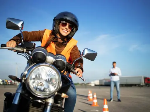 Uśmiechnięta kursantka na motorze, w kamizelce odblaskowej i kasku, uczy się jeździć. Zastanawiasz się, ile kosztują prawo jazdy na motor?