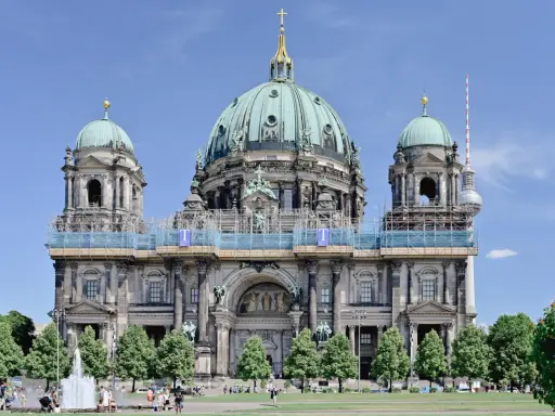 Berlins domkyrka med sina imponerande kupoler är ett måste när man undrar vad ska man se i Berlin. En fontän och grönskande träd ramar in den vackra byggnaden.