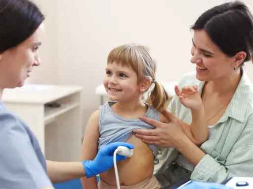 Lekarz wykonuje usg brzuszka niemowlaka. Uśmiechnięta dziewczynka i jej mama towarzyszą badaniu.
