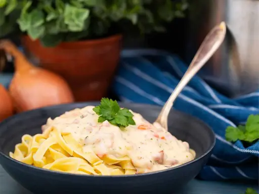 En skål med tagliatelle täckt av krämig ost och skinksås, toppad med persilja. En gaffel sticker upp ur pastan.