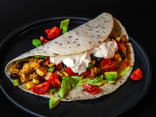 Ein köstliches Fajitas-Rezept: Tortilla gefüllt mit Hähnchen, Gemüse, Avocado und Sour Cream, garniert mit Tomaten.