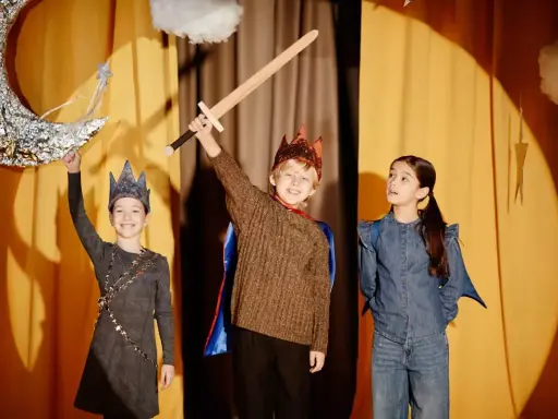 Niños en un escenario, listos para obras de teatro para niños. Uno sostiene una espada, otro una luna y una varita mágica.
