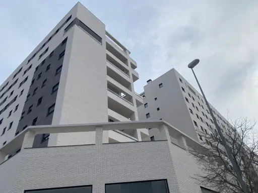 Modernas viviendas VPO en Alicante, edificios de ladrillo blanco y gris con balcones, bajo un cielo nublado.