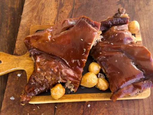 Delicioso cochinillo al horno, crujiente y jugoso, servido con patatas asadas sobre tabla de madera.