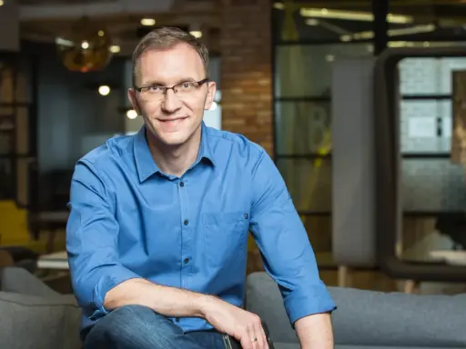 Marcin Iwuć, twórca "Finansowej fortecy", w niebieskiej koszuli siedzi na kanapie, uśmiechając się do obiektywu.