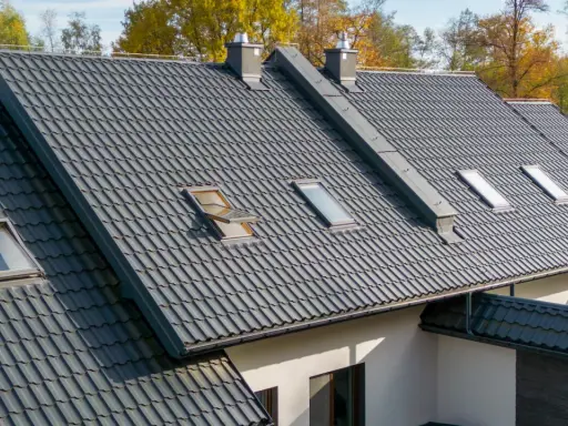 Szeroki dach pokryty ciemnoszarymi dachówkami ceramicznymi, z kilkoma oknami dachowymi i kominami. Różne rodzaje dachówek tworzą harmonijną całość.