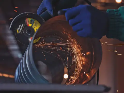 Manos enguantadas usan una radial para cortar un tubo, generando chispas. Un accidente con radial es un riesgo constante.