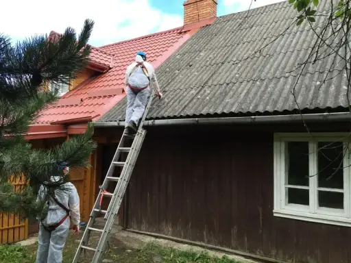 Pracownicy w kombinezonach zabezpieczających usuwają eternit z dachu. To pokazuje, co to jest azbest i jak wygląda jego utylizacja.
